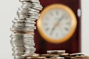 A stack of coins in front of a clock.