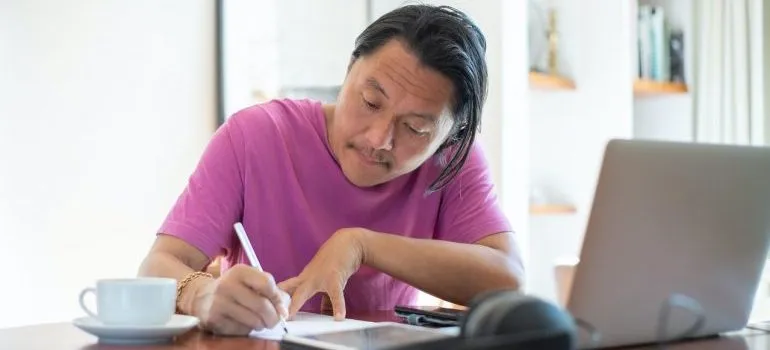 Man in front of laptop writing down something - There are many great online resources available that can help you find a job in Hong Kong.
