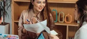 two women smiling and holding papers