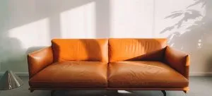 A two seat orange sofa against the wall, as someone is considering what's the cheapest way to move furniture.