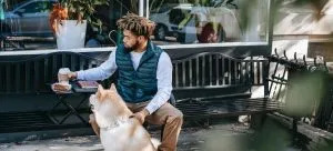 Black man with coffee on bench near dog