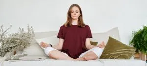 A woman in a red shirt meditating on a couch to deal with the emotional rollercoaster after relocating from Hong Kong