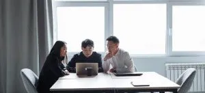 three people sitting and looking at the laptop