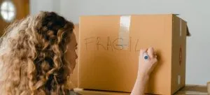 A woman writing "FRAGILE" on a box before HK furniture shipping.