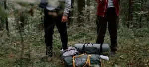 Two persons standing in the forest with their camping gear.