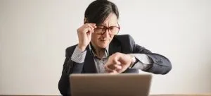 A man in front of a laptop looking at watch.